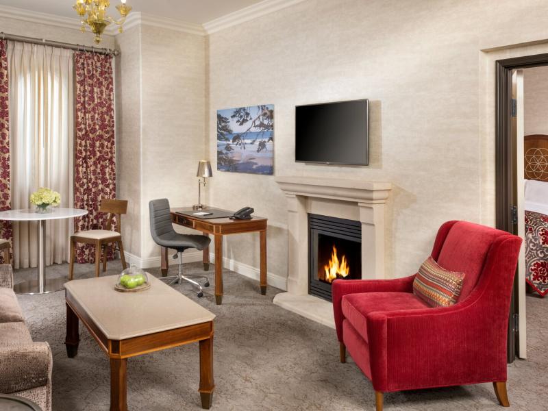 This inviting One Bedroom King Fireplace Suite features a cozy fireplace, separate living area, and classic furnishings accented with rich red upholstery, warm wood tones, and soft neutral creams.