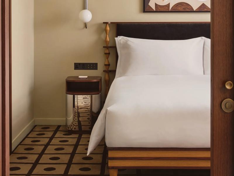 One-Bedroom Suite detail highlights crisp white linens, a sleek nightstand, and patterned tile flooring, complemented by natural wood finishes, muted tan walls, and black accents