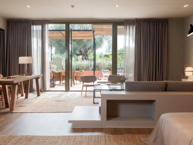 The Presidential Suite bright, open layout blends natural wood tones with soft gray textiles, framed by expansive glass doors that reveal lush greenery and warm terracotta accents of it’s private terrace.