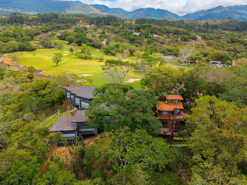 An elevated aerial view of Lucero Residences Golf & Wellness Resort reveals Treehouses Canopy Suites nestled among lush greenery beside a vibrant golf course, blending rich forest greens with natural browns and charcoal gray rooftops.