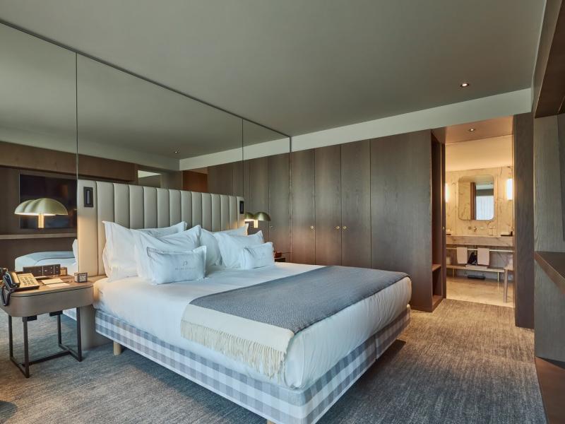 Rooftop suite bedroom with upholstered bed, mirrored wall, and marble bathroom at Altis Porto Hotel