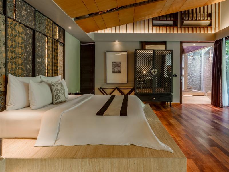 The Imperial Villa elegant bedroom showcases a handcrafted king bed, textured accent wall, and indoor–outdoor layout highlighted by creamy white linens, honeyed wood, and subtle bronze details.