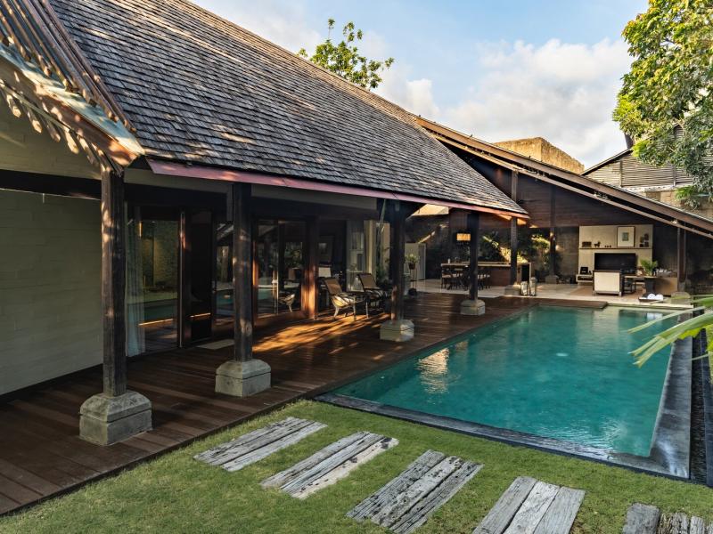 The Imperial Villa exterior wraps around a private pool and timber deck, blending contemporary lines with natural materials in shades of teak brown, jade green, and cool blue.