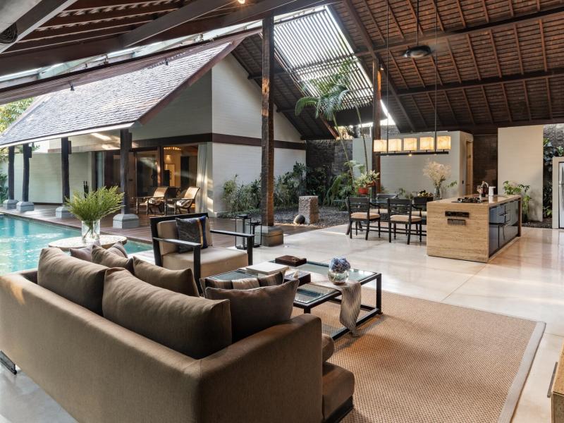 The Imperial Villa expansive open-plan living space flows seamlessly to a private pool, featuring plush lounge seating, warm wood beams, and accents of soft taupe, charcoal, and tranquil aqua.