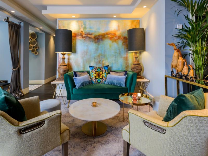 The Victoria Killarney elegant lobby lounge space is anchored by a velvet emerald sofa, sculptural armchairs, and art-led décor, accented with brushed gold, soft neutrals, and rich teal hues.
