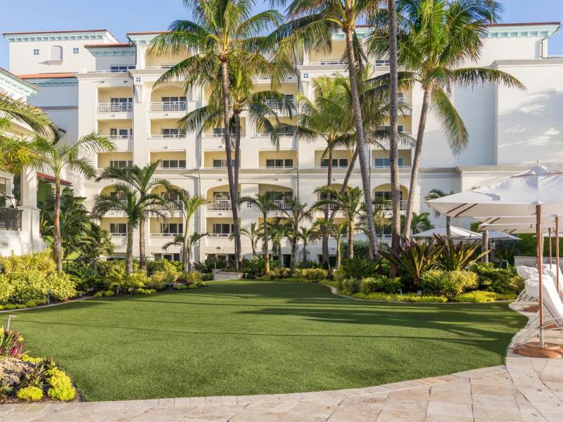 Eau Resort & Spa serene lawn offers manicured greenery, resort-style loungers, and tropical palms, complemented by fresh green hues, creamy whites, and sunlit beige stone accents.