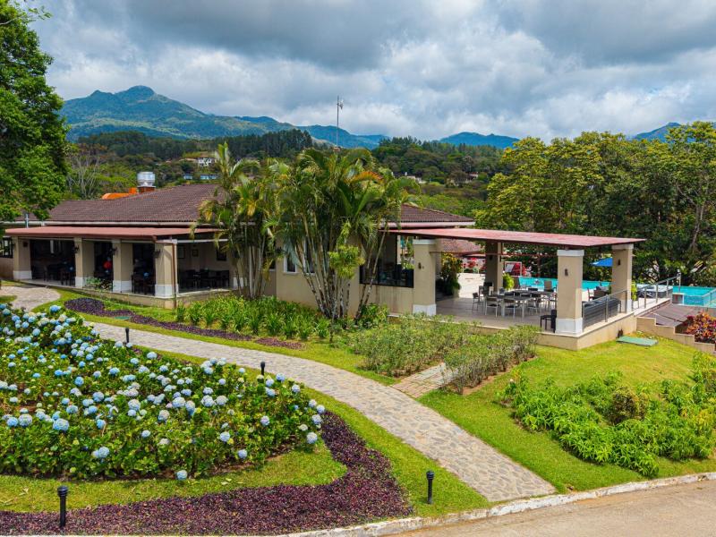 Seasons Restaurant’s terrace features open-air dining, landscaped gardens, and scenic hillside views, complemented by lush greens, soft cream walls, and terracotta roof accents.