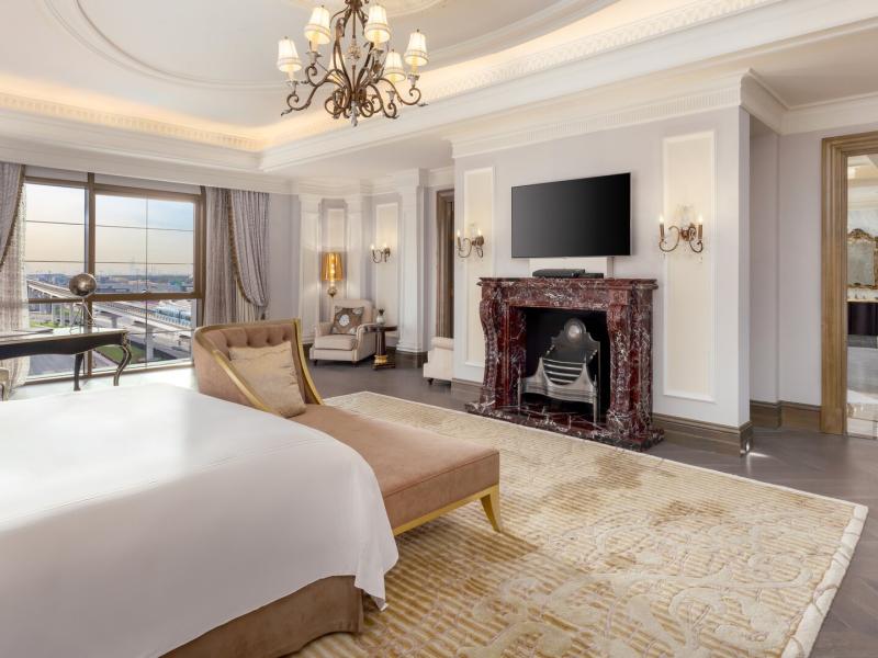 This refined bedroom of the Sir Winston Churchill Suite pairs a marble fireplace and expansive city views with tailored furnishings in warm beige, ivory, and subtle brass accents.