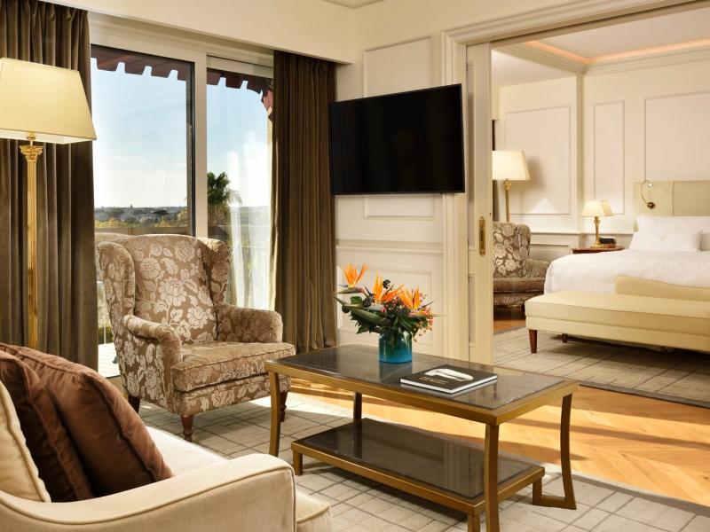 The inviting Executive Park View Suite combines a comfortable sitting area, sleek furnishings, and an open bedroom layout, enhanced by beige, chocolate brown, and subtle gold accents.