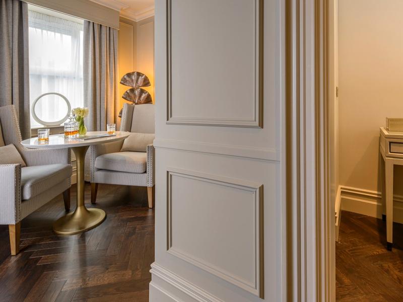 A refined sitting area in a Arbutus Suite with tailored armchairs, a sculptural brass table, and soft drapery is finished in warm taupe and ivory with elegant gold accents.