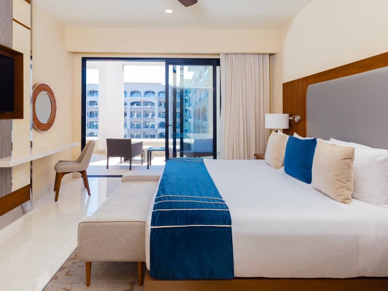 Villa La Valencia Beach Resort & Spa’s One Bedroom Suite Pool View serene retreat features a comfortable king bed, integrated work desk, and balcony access, styled with crisp white linens, rich blue accents, and warm wood details.