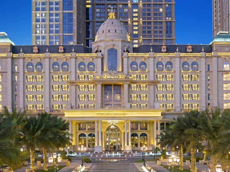 Al Habtoor Palace Dubai’s majestic palace façade glows at night with grand arched colonnades, illuminated windows, and formal palm‑lined gardens, accented in warm golden light, soft champagne stone, and deep sapphire‑blue skies.