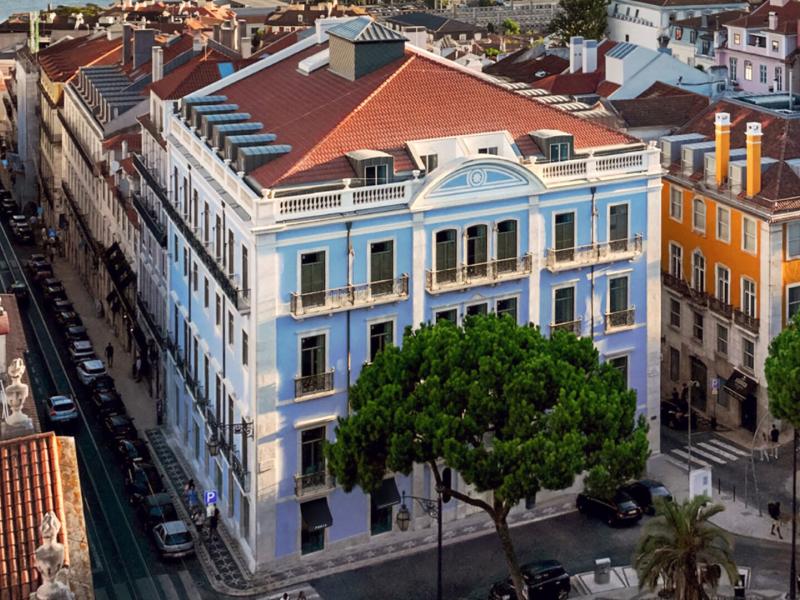 Montebelo Vista Alegre Lisboa Chiado Hotel’s soft blue façade, wrought‑iron balconies, and terracotta rooflines, accented by crisp white detailing and lush emerald greenery.