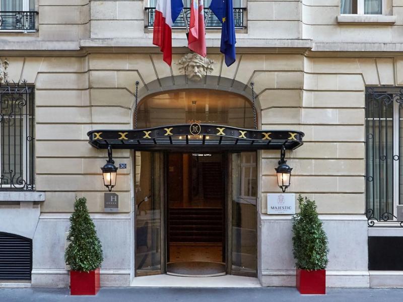 Majestic Hotel-SPA Champs-Elysées classic Parisian-style façade highlighted by a revolving entrance, wrought-iron details, and topiary planters, complemented by stone gray architecture with black and gold accents.
