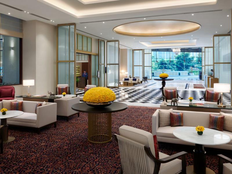 The elegant lobby lounge at The Leela Bhartiya City offers plush seating, sculptural lighting, and garden views, elevated by refined accents of cream, ruby red, and warm bronze.