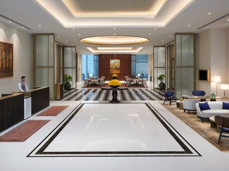 The Leela Bhartiya City grand, light-filled lobby showcases marble floors, contemporary seating, and artful details accented in warm ivory, deep wood tones, and hints of gold.