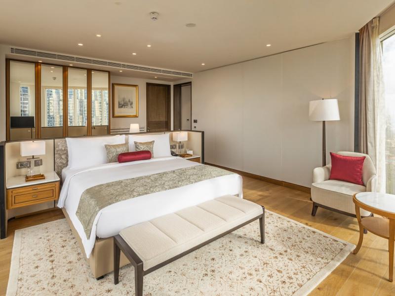 The serene bedroom of a Luxury Suite offers a lavish king bed, bespoke furnishings, and expansive windows, layered in calming shades of pearl ivory, champagne gold, and pale natural wood.