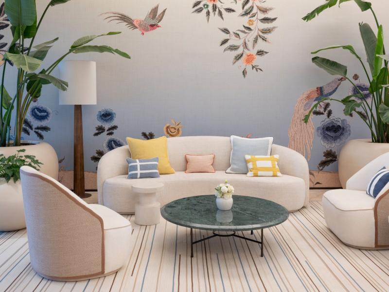Elegant lobby lounge seating pairs sculptural cream seating, a green marble coffee table, and botanical murals accented in soft blush, sage green, and muted blue.