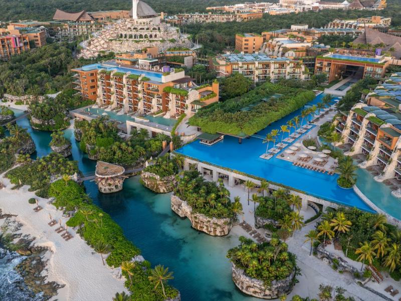 Hotel Xcaret Arte grand coastal haven features radiant sapphire waterways, pristine ivory sands, and elegant ochre villas nestled within lush emerald jungle landscapes.