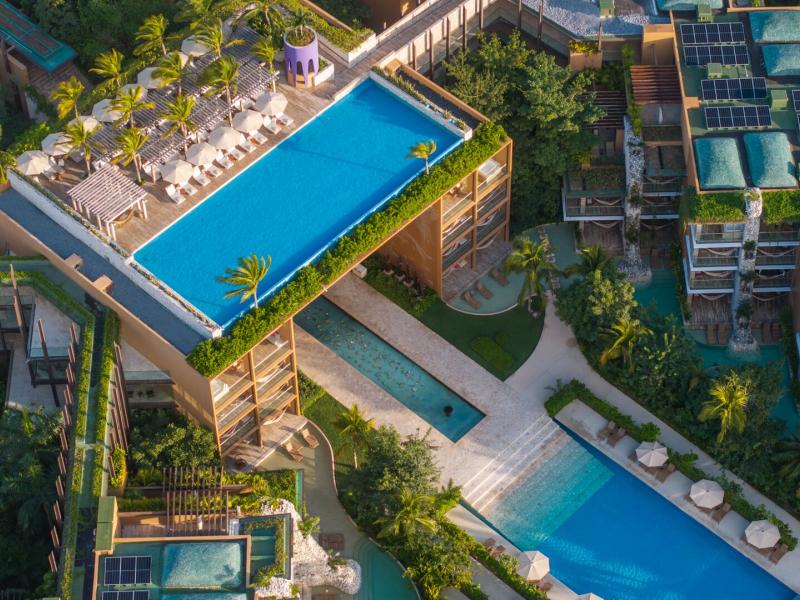 The ultra-luxurious multi-level resort showcases a striking infinity-edge pool, sleek sun loungers, cascading lower pools, and lush tropical terraces in vibrant turquoise, deep emerald, and warm sand tones.