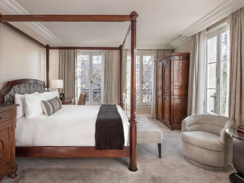 A grand and light-filled Luxe Guestroom retreat showcases a statement four‑poster bed, bespoke cabinetry, and graceful French doors dressed in creamy neutrals, elevated by deep espresso wood and misty gray textiles.