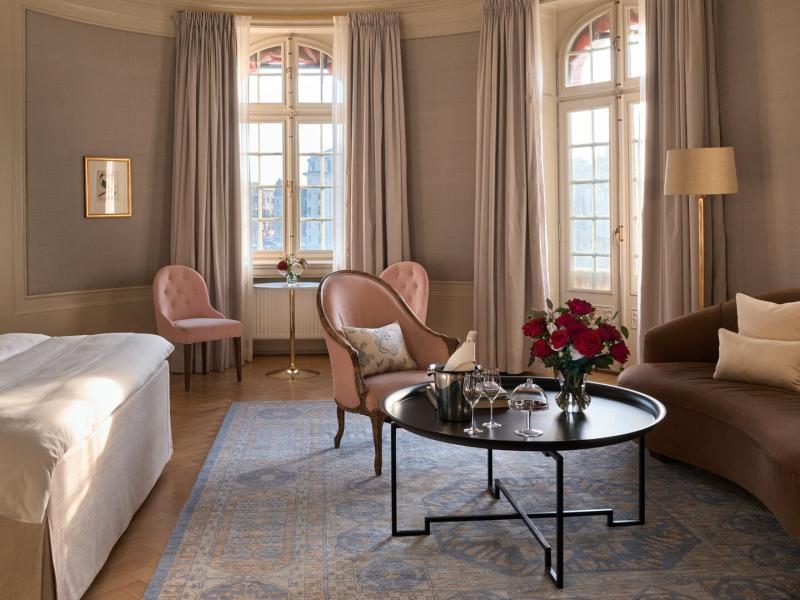 This sophisticated Dagmar Master Suite pairs soaring windows, bespoke seating, and plush furnishings with soft blush, taupe, and champagne tones.