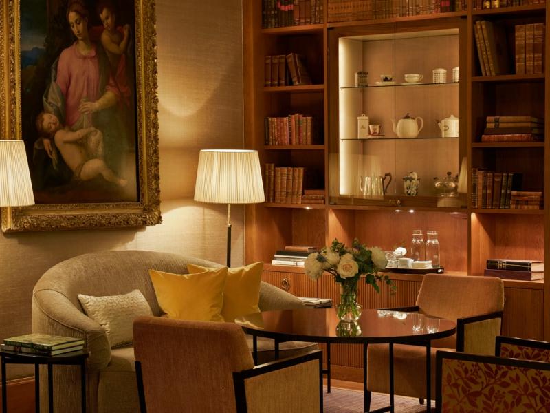 The intimate Library features rich walnut bookshelves, bespoke lounge seating, and warm gold and ivory accents beneath soft ambient lighting.