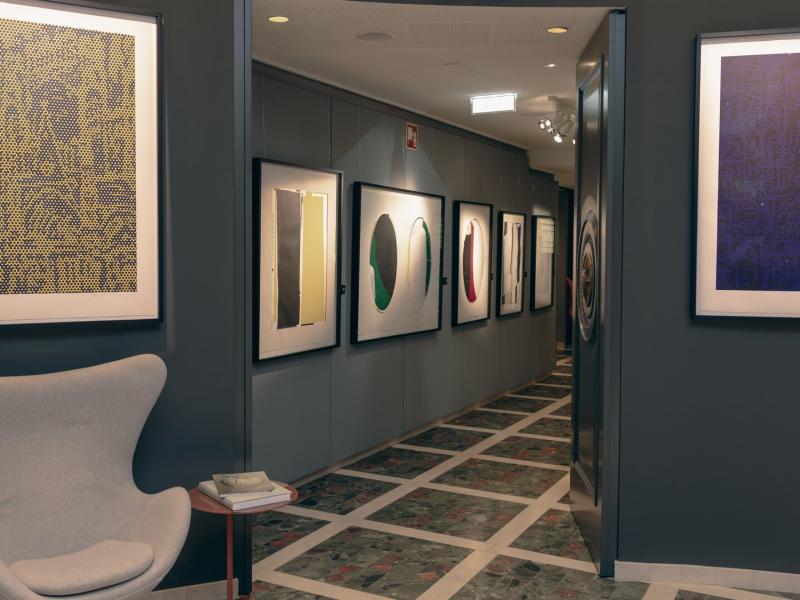 This stylish corridor at Hotel Sans Souci Wien features curated modern artwork, geometric marble flooring, and sophisticated navy and ivory tones accented with vibrant emerald and ruby details.