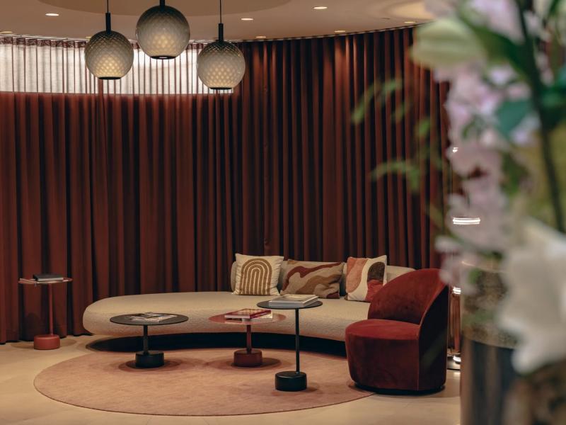 The hotel’s lobby unveils an intimate lounge adorned with sculptural lighting, plush curved seating, and rich burgundy and ivory accents for a sophisticated retreat.
