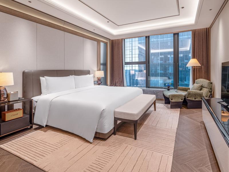 This elegant Peak View Zunyue Two-Bedroom Suite offers a plush king bed, inviting lounge seating, and sophisticated beige, walnut-brown, and soft blue tones overlooking the cityscape.