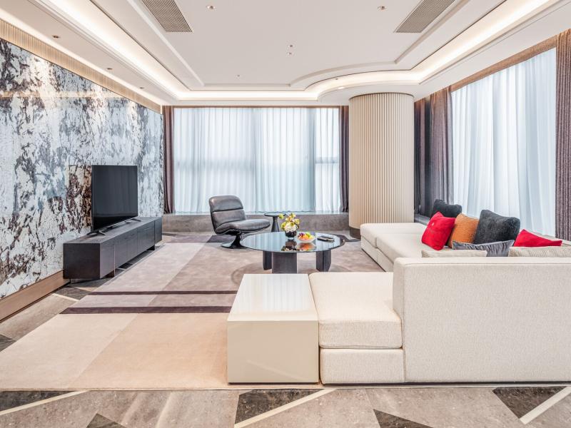 A Peak View Zunyue Two-Bedroom Suite sophisticated living room showcases a dramatic marble feature wall, plush ivory seating, and elegant charcoal accents enhanced by vibrant ruby-red touches.