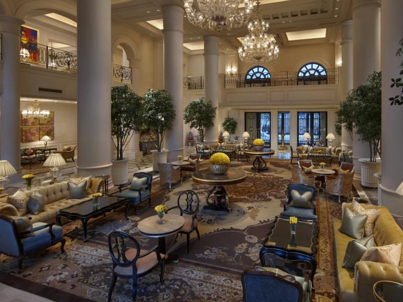 The Leela Palace New Delhi palatial lobby captivates with soaring ivory columns, sparkling crystal chandeliers, and elegant furnishings accented in soft gold, navy blue, and cream.