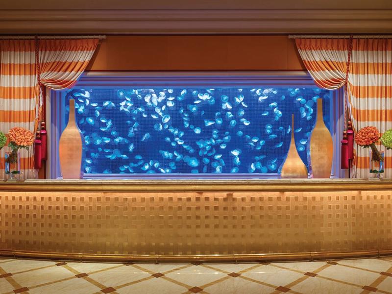 Wynn Macau and Encore glowing gold lobby reception desk, vibrant blue jellyfish aquarium, and elegant orange-and-white drapery create a captivating welcome rich in warm amber hues.