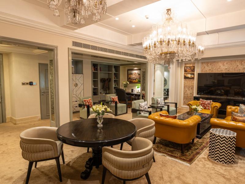 The Presidential Suite features dazzling crystal chandeliers illuminating mustard leather sofas, sage armchairs, a dark-wood dining table, curated artwork, layered rugs, and a refined private study.