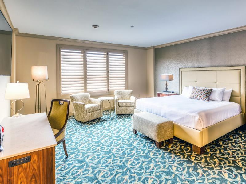 This Valley Tower guest room features a plush upholstered bed, elegant sitting area, refined walnut furnishings, and soothing blue-and-ivory accents.