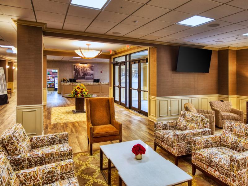 The Valley Tower lobby showcases a lounge with warm palette of rich browns, ivory accents, and patterned seating, where plush gathering spaces, glowing chandeliers, and elegant décor create a welcoming sense of timeless luxury.