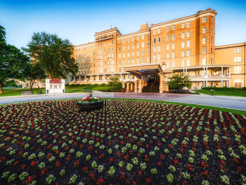 The French Lick Springs Hotel is framed by vibrant red-and-white gardens, manicured emerald lawns, it’s grand historic architecture glowing beneath a sapphire sky, this legendary resort embodies classic luxury and enduring charm.
