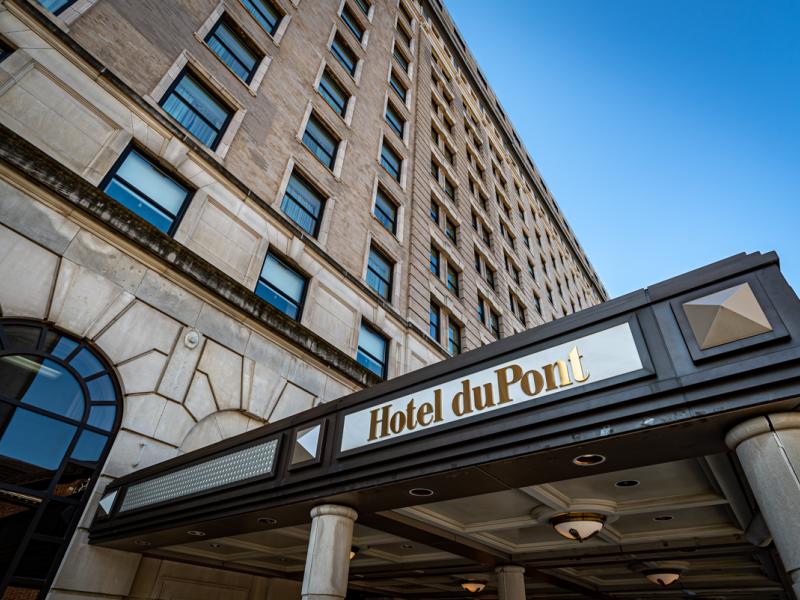 HOTEL DU PONT elegant entrance features a sculpted glass canopy and warmly lit stone façade accented with deep bronze and gold tones.