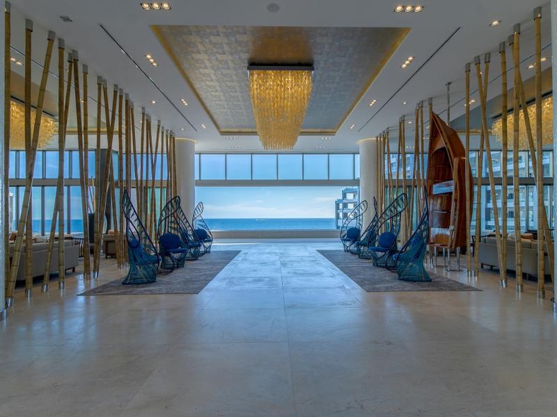 The luxurious oceanfront lobby features elegant chandeliers, artistic seating, and floor-to-ceiling windows framing a stunning view of the sea.