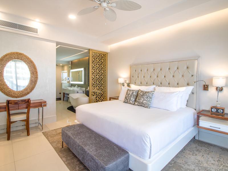 one Bedroom Suite, modern bedroom features a plush king-sized bed with a tufted headboard, elegant decor, and an open view into a luxurious bathroom.