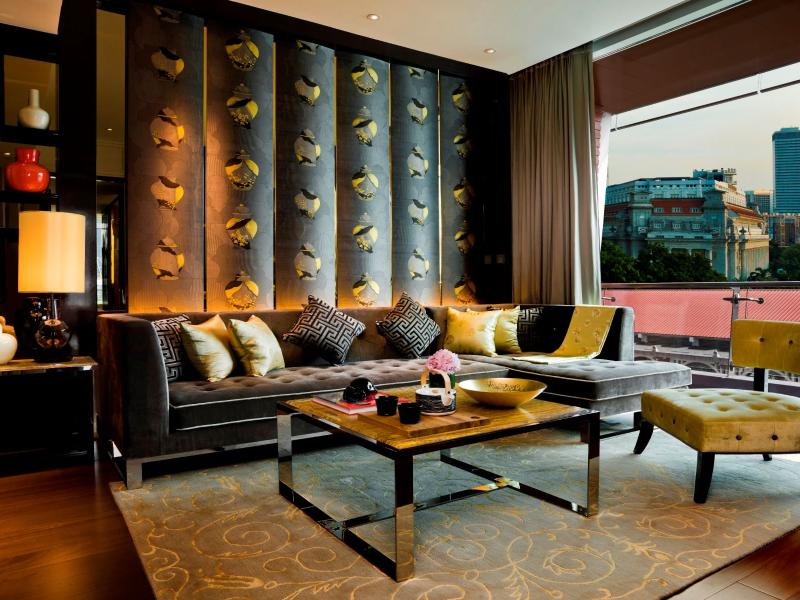 The Robinson Suite elegant living room showcasing a tufted sofa, patterned feature wall, and modern coffee table, brought together with charcoal gray seating, gold details, and rich brown wood accents.