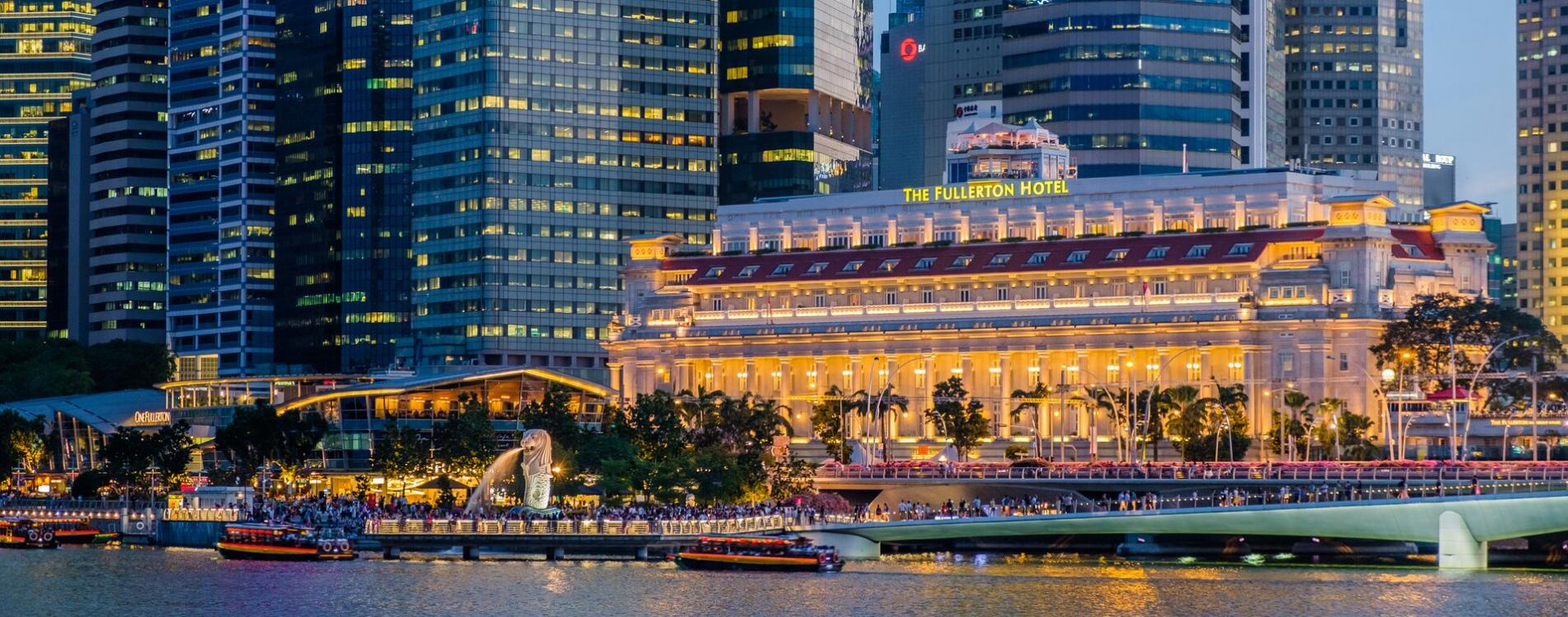 The Fullerton Hotel Singapore with boats in harbor at night