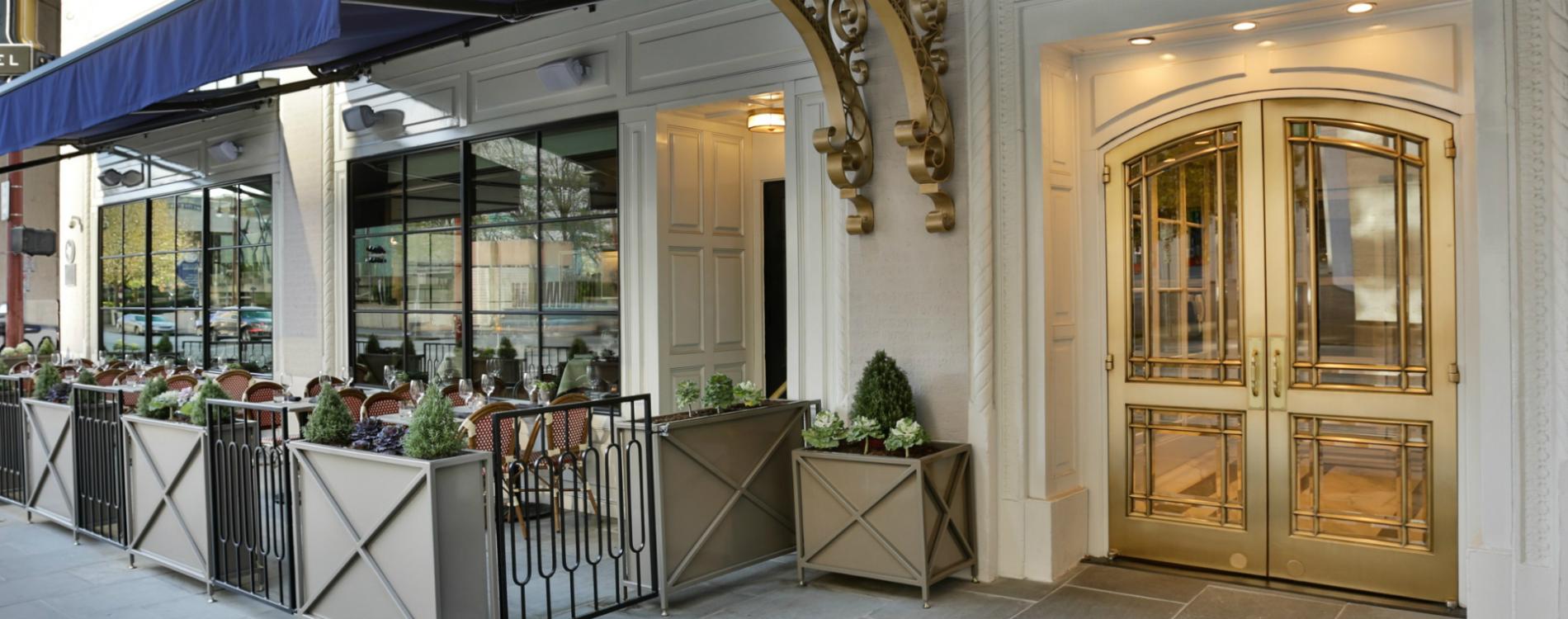 A restaurant entrance with a glass door, outdoor seating, and plants